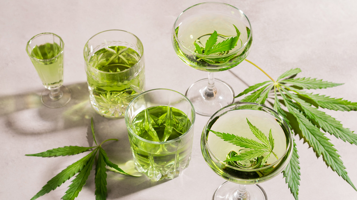 Vari bicchieri di bevande verde pallido alla cannabis, guarniti con foglie fresche su superficie bianca
