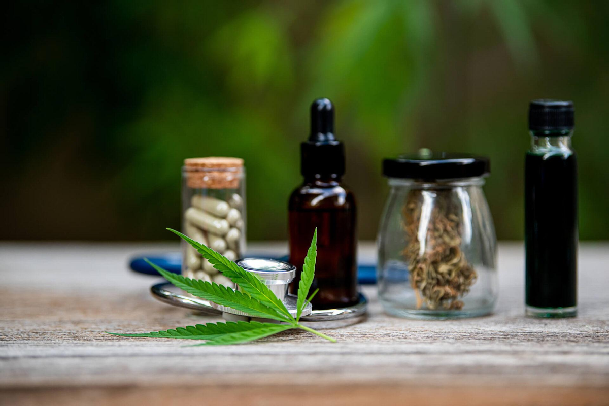 Foglia di cannabis con vari metodi di consumo, tra cui tinture all'olio, fiori essiccati, capsule e cartucce vape