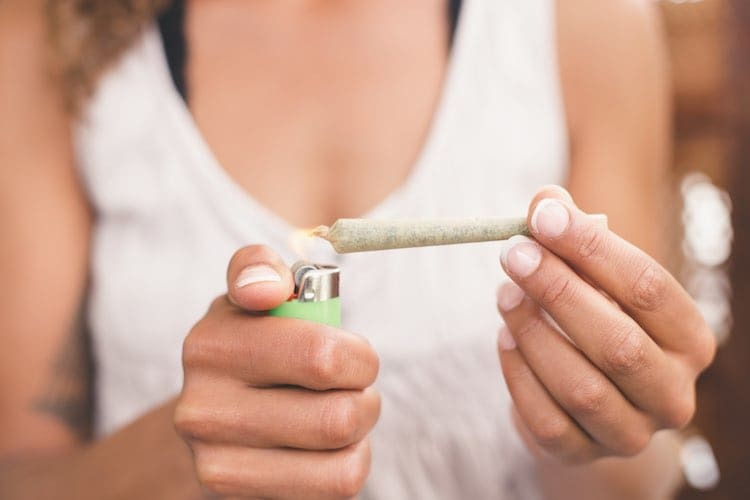 Persona che tiene un joint acceso con un accendino verde in una scena lifestyle
