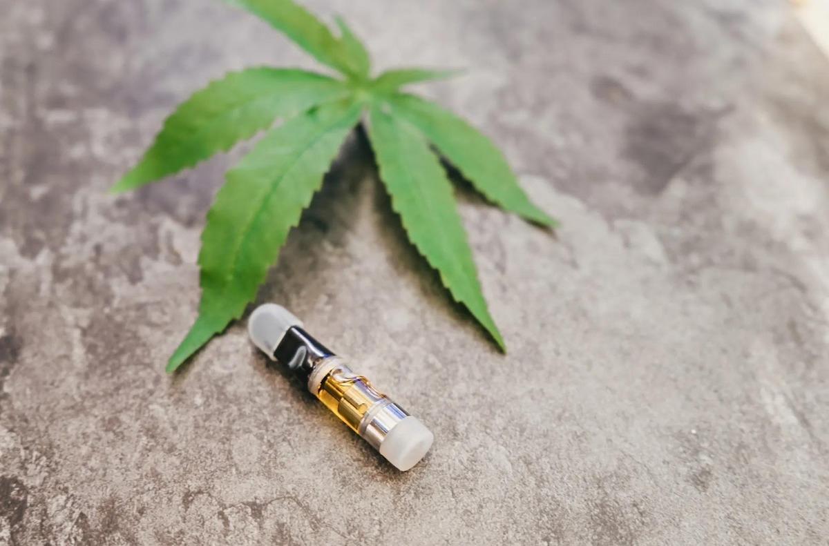 Foglia di cannabis e cartuccia vape su superficie di cemento