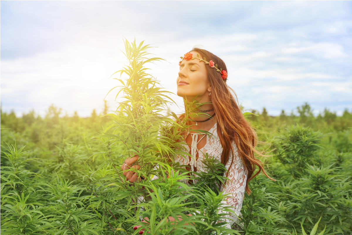 Donna con corona di fiori in un campo di cannabis in fiore sotto il cielo azzurro